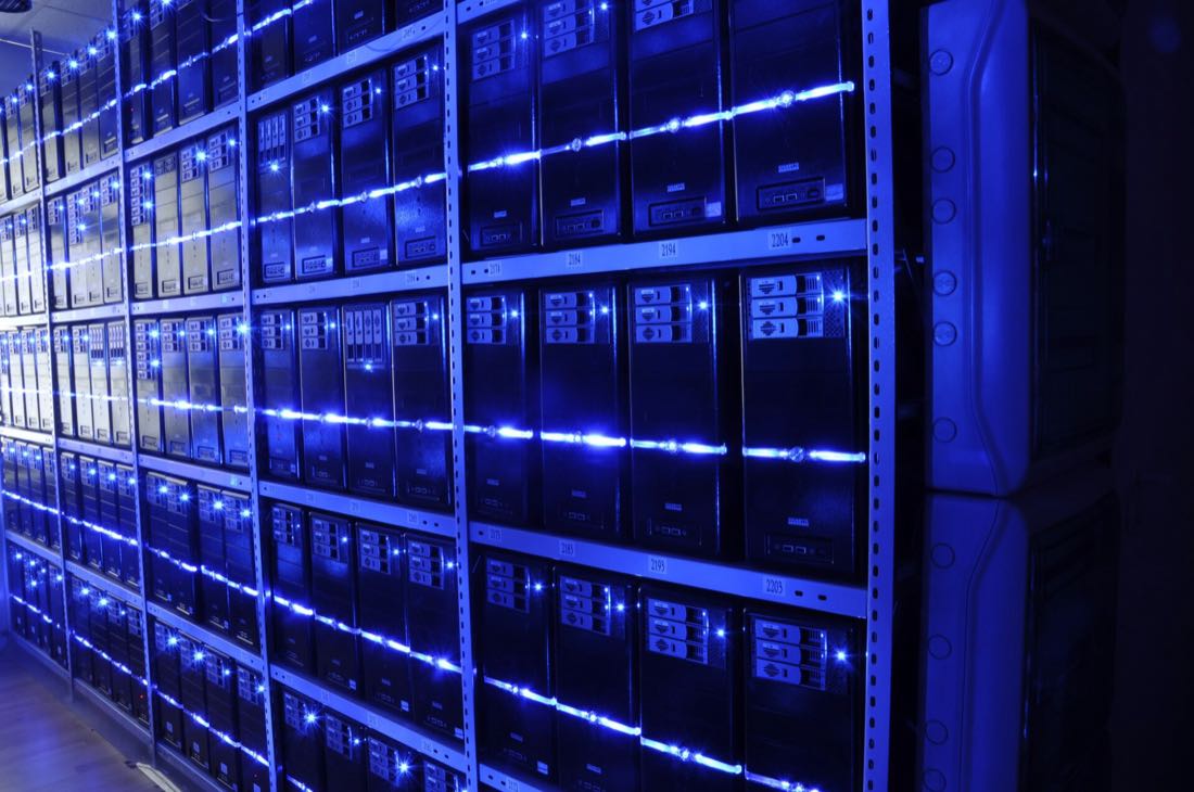 Rows of server racks with blue lights in a data center aisle.